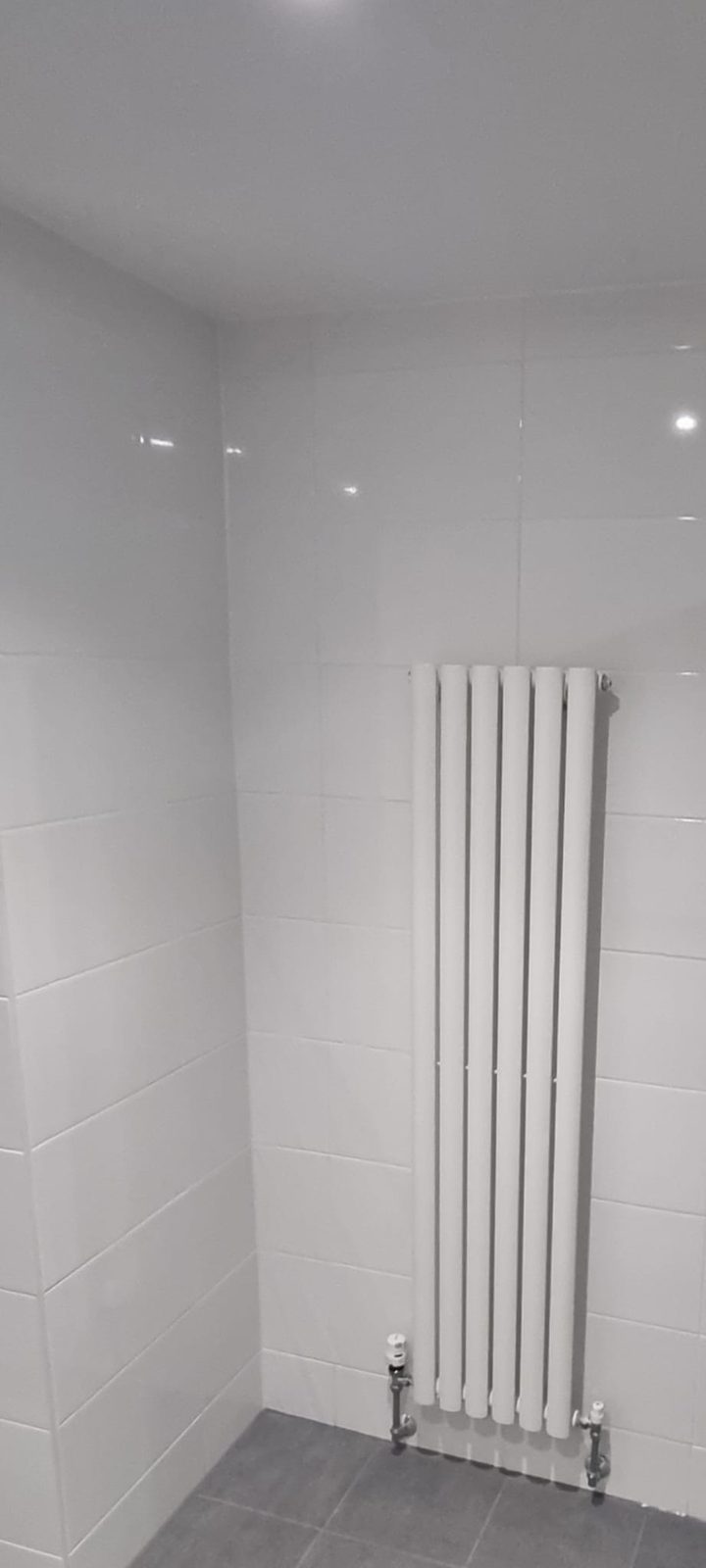 Vertical column radiator fitted neatly in a newly tiled bathroom